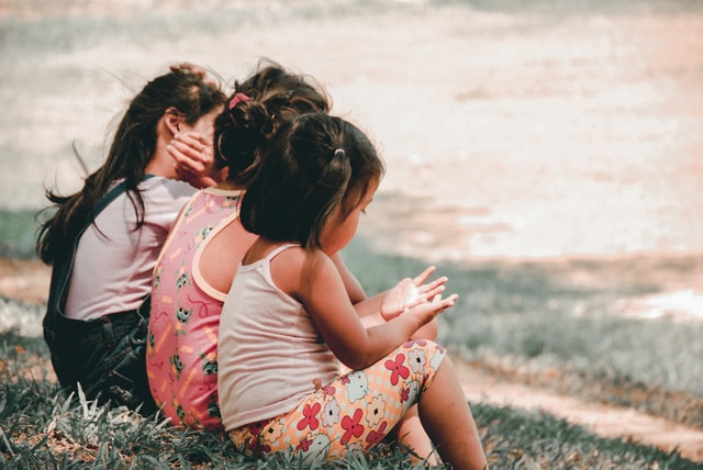 Three young girls sitting on the grass looking at their phones.